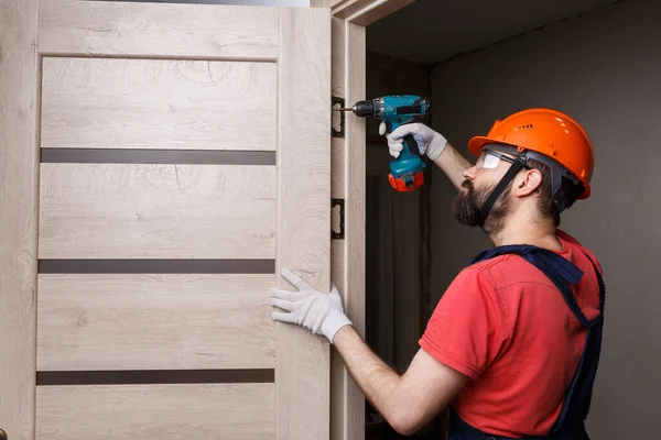 Turuncu kasklı matkaplı bir işçi eve bir kapı yerleştirir.