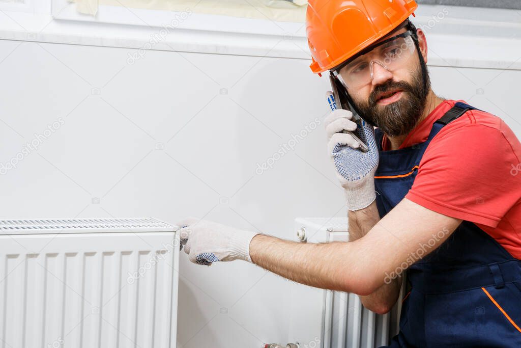 a worker in an orange helmet installs radiators in the house