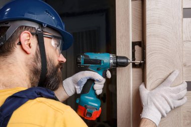 Turuncu kasklı matkaplı bir işçi eve bir kapı yerleştirir.