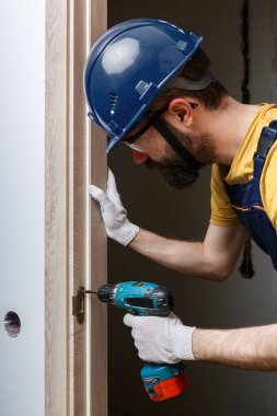 Turuncu kasklı matkaplı bir işçi eve bir kapı yerleştirir.