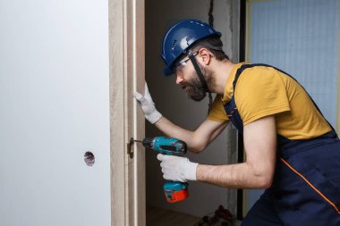 Turuncu kasklı matkaplı bir işçi eve bir kapı yerleştirir.