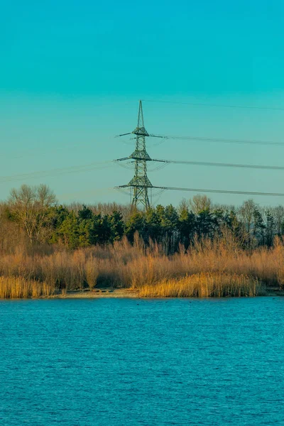 Réseau Électrique Atteignant Forêt Par Lac Bleu Décor Éclairé Par Image En Vente