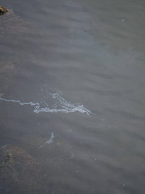 Kumsaldaki turkuaz denizin yüzeyinde kirli yağlı film. Endüstriyel atık su sızıntısı. Yağ film kirliliği. Suyun üstünde renkli bir yağ filmi. endüstriyel atık su sızıntısı. denizdeki gökkuşağı