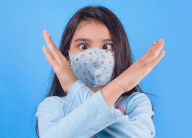 portrait of young woman wearing medical mask and gloves holding hands on her face against blue background