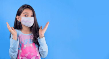 Mavi arka planda tıbbi maske takan ve koruyucu eldiven takan genç bir kadın.