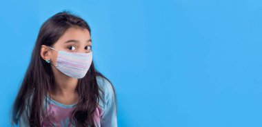 Tıbbi maske ve mavi gömlek giyen genç bir kadın, kameraya bakıyor, beyaz arka planda izole edilmiş.