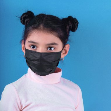 Koruyucu maske takan genç bir kadının portresi ve gri arka planda mavi bir eşarp.