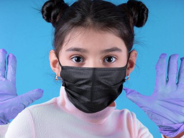 Mavi arka planda koruyucu maskeli genç bir kadının portresi.