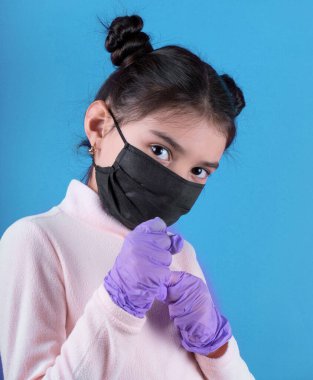 Mavi arka planda koruyucu maskeli ve eldivenli genç bir kadın.