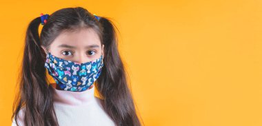 Sarı yağmurluklu ve arka planda örülmüş şapkalı koruyucu yüzlü bir kız..