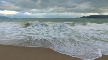 Deniz dalgası sahildeki kumu yıkar. Bulutlu hava