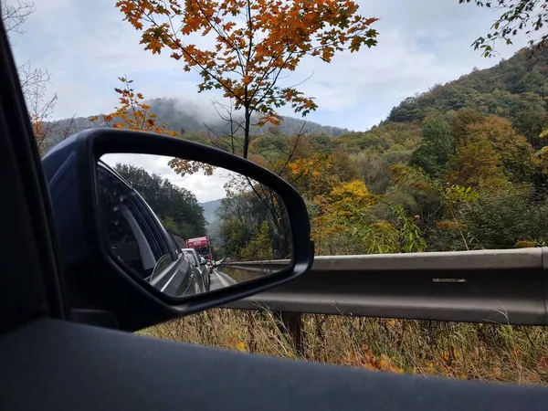 秋の山の森の中で自動車と道路上の車のミラーからの眺め — ストック写真
