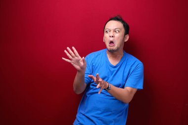 Genç Asyalı adam şaşırmış ve kızgın kırmızı arka planda izole edilmiş gibi görünüyor..