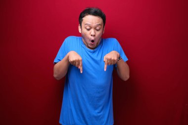 Genç Asyalı adam şaşırmış ve elleri kırmızı arka planda bağırıyor..