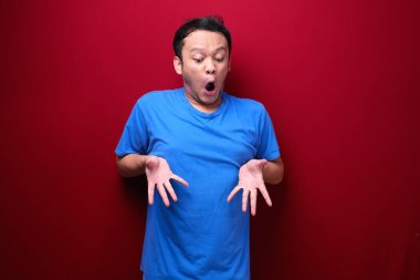 Genç Asyalı adam şaşırmış ve elleri kırmızı arka planda bağırıyor..