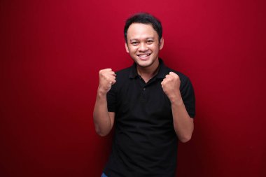 Mutlu ve gülümseyen Asyalı genç adam başarı ve başarıyı kutlamak için kolunu kaldırıyor..