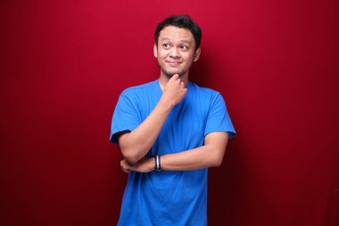 Genç Asyalı adamın kırmızı arka planda ciddi bir jest yaptığını düşünüyorum.