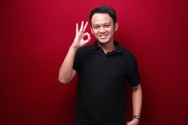 Gülümseyen yüzü ve baş parmağı olan mutlu Asyalı genç adam ya da tamam işareti