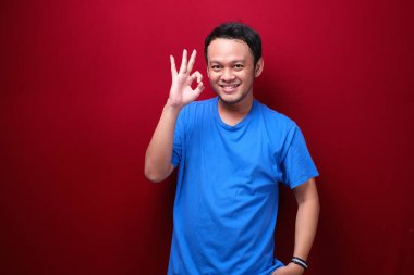 Gülümseyen yüzü ve baş parmağı olan mutlu Asyalı genç adam ya da tamam işareti