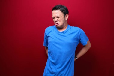 Üzgün ve üzgün Asyalı bir adam. Sırtında ciddi bir ağrı var.