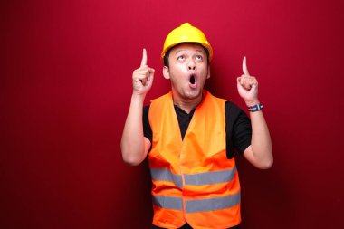 Şok Genç Asyalı işçi şaşırdı ve haykırıyor elleri kırmızı arka planda izole bir şekilde yukarıyı işaret ediyor..