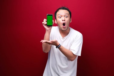 Şok Genç Asyalı adam kırmızı arka planda yeşil boş alanı işaret ediyor..