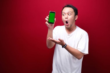 Şok Genç Asyalı adam kırmızı arka planda yeşil boş alanı işaret ediyor..