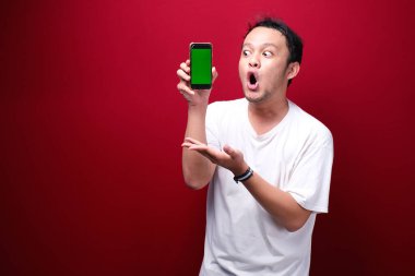 Şok Genç Asyalı adam kırmızı arka planda yeşil boş alanı işaret ediyor..