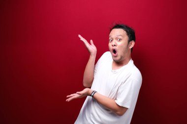 Genç Asyalı adam şaşırmış ve haykırıyor elleri kırmızı arka planda izole bir şekilde sağa dönük..
