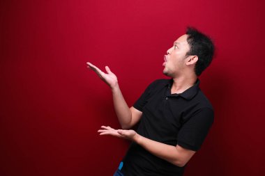 Genç Asyalı adam şaşırmış ve haykırıyor elleri kırmızı arka planda izole bir şekilde sağa dönük..