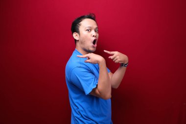 Genç Asyalı adam şaşırmış ve haykırıyor elleri kırmızı arka planda izole bir şekilde sağa dönük..