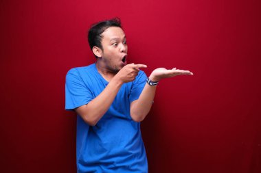 Genç Asyalı adam şaşırmış ve haykırıyor elleri kırmızı arka planda izole bir şekilde sağa dönük..