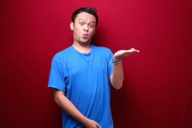 Genç Asyalı adam şaşırmış ve haykırıyor elleri kırmızı arka planda izole bir şekilde sağa dönük..