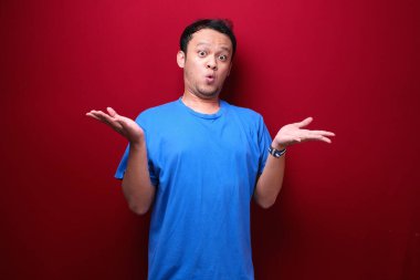 Genç Asyalı adam şaşırmış ve haykırıyor elleri kırmızı arka planda izole bir şekilde sağa dönük..