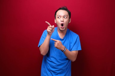 Genç Asyalı adam şaşırmış ve haykırıyor elleri kırmızı arka planda izole bir şekilde sağa dönük..