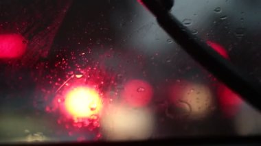 Arabanın ön camına yağmur yağıyor. Trafik sıkışıklığında trafik sıkışıklığında araba sür. Şiddetli yağmur fırtınasında, bir arabanın içinde sür. Trafik lambası arkaplanı bulanık..