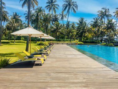 Şemsiyeli otel veya tatil beldesinde güzel tropikal yüzme havuzu, hindistan cevizi ağacı şezlongları, sonsuzluk havuzu manzaralı palmiye ağaçları, okyanus ve dağ arka planı.