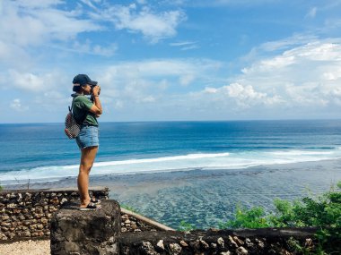 Gunung Payung Sahili, Nusa Dua, Bali, Endonezya 'da fotoğraf çekmek için bekleyen genç bir kadın yolcu harika bir okyanus ve sahil manzarası var..
