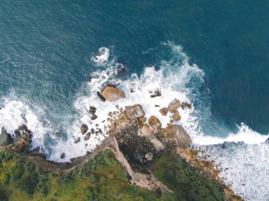 Okyanus dalgalarının mercan plajına çarpıp köpürmesini gösteren tepeden aşağı hava manzarası.