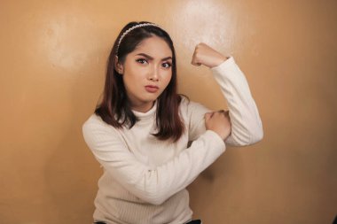 Beyaz gömlekli, pazılarını gösteren ve gülümseyen muhteşem güçlü Asyalı kadın. Endonezyalı kız güçlü konsept.