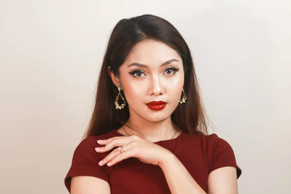 A fierce-looking Asian woman in a red shirt posing in front of white background