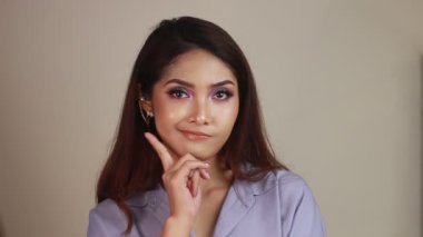 Gri arka planda uzun saçlı ve beyaz gömlekli güzel bir genç kadın.