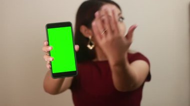 Genç ve güzel bir kadın elinde boş ekranlı akıllı telefon tutuyor, yeşil ekranda izole edilmiş.