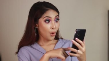 Asyalı güzel kız beyaz gömlekli akıllı telefondan şoke oldu.