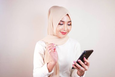 Cep telefonuna bakarken gülümseyen neşeli, genç Müslüman Asyalı kadının portresi.