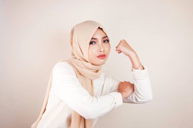 Beyaz arka plan duvarında bisepslerini gösteren muhteşem, güçlü, genç Müslüman kadın..