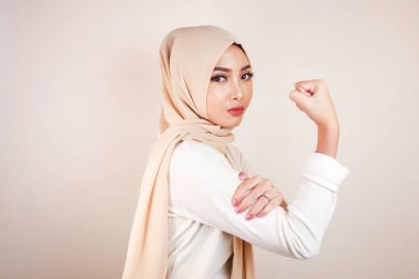 Beyaz arka plan duvarında bisepslerini gösteren muhteşem, güçlü, genç Müslüman kadın..