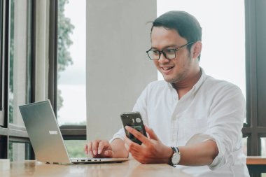 Young Asian businessman talking on a smartphone at a desk at caffe