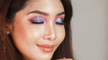 Profesyonel makyajlı, parlak tenli ve koyu renk saçlı güzel bir Asyalı kız. Renkli dumanlı gözler.
