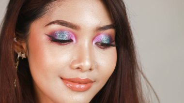 Profesyonel makyajlı, parlak tenli ve koyu renk saçlı güzel bir Asyalı kız. Renkli dumanlı gözler.